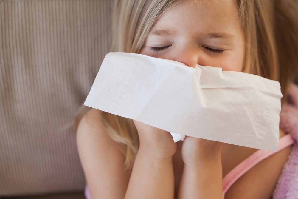 A little girl blowing her nose into a tissue