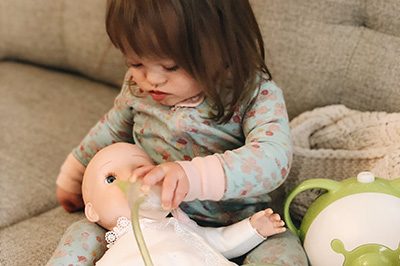 A little girl is pretending to clean the nose of her doll with a Nosiboo Pro electric nasal aspirator 