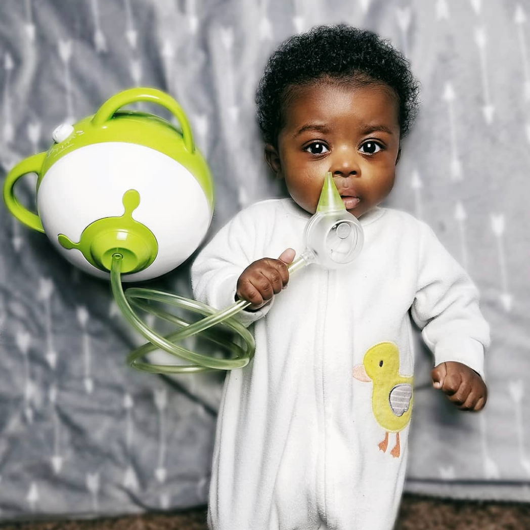 A lying baby holding a Nosiboo Pro electric nasal aspirator