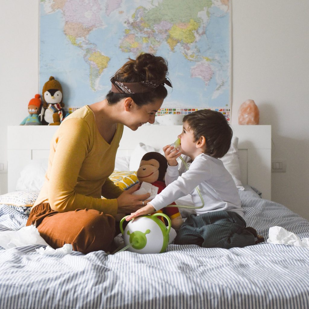 Mom with her son sitting on a bed, aspirating the child's nose with a Nosiboo Pro electric nasal aspirator