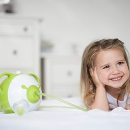 A little smiling girl lying on her bed next to the Nosiboo Pro Electric Nasal Aspirator