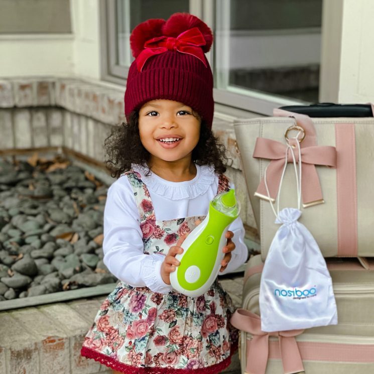 A beautiful, stylish little girl in a red winter hat holding the Nosiboo Go Portable Nasal Aspirator in her hands